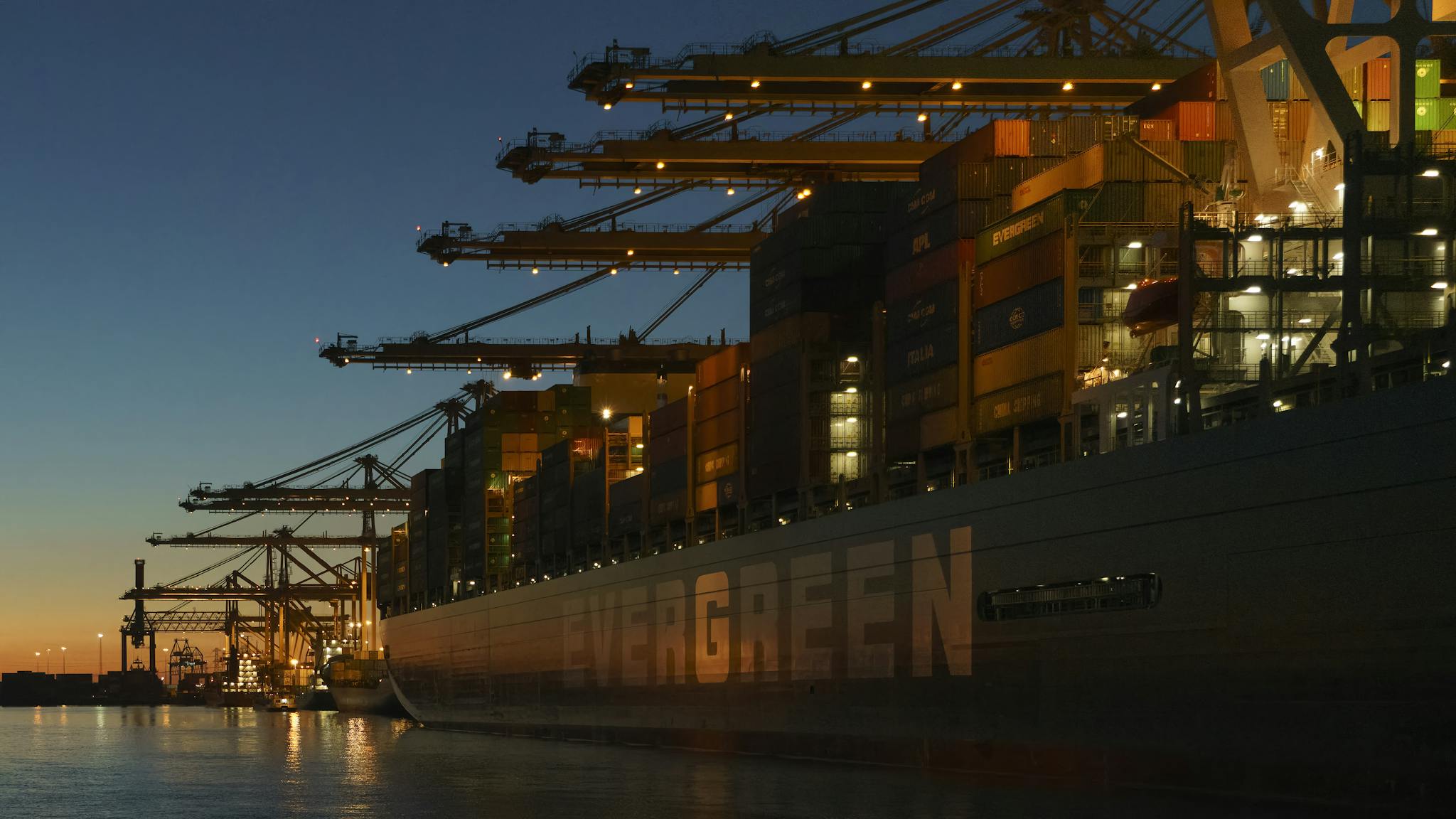 Large container ship docked at Rotterdam harbor with cranes at twilight.